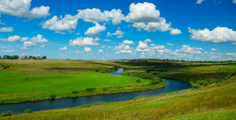 Fototapeta na wymiar Sunny summer scene with river curve,fields,green hills,distant woods and beautiful clouds in blue sky.