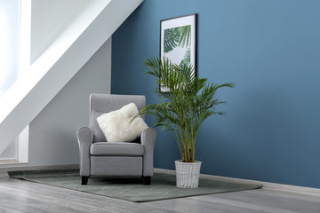 Comfortable armchair with houseplant near color wall in room