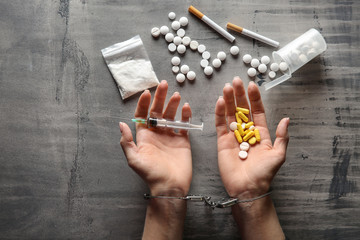 Female junkie in handcuffs with drugs and syringe on grey background. Concept of addiction