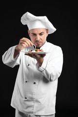 Male chef with tasty salad on dark background