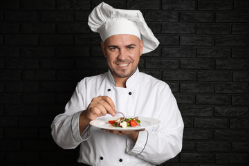 Male chef with tasty salad on dark background