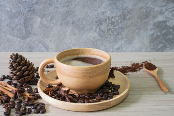 Black hot coffee in wooden cup and wooden spoon with cinnamon, pumpkins and star anise and coffee beans and on wooden background