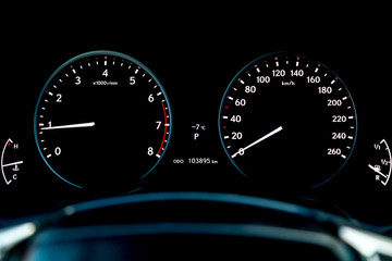 Close-up of a car dashboard with a tachometer and speedometer indicating fuel level and measuring engine speed and speed against a black background.