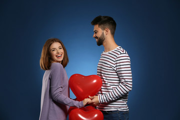 Loving young couple with heart-shaped balloons on color background. Celebration of Saint Valentine's Day