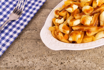 Poutine plate on a concrete background. Cooked with french fries, beef gravy and curd cheese. Canadian cuisine.