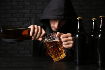 Man pouring beer into glass at table near black brick wall. Alcoholism concept