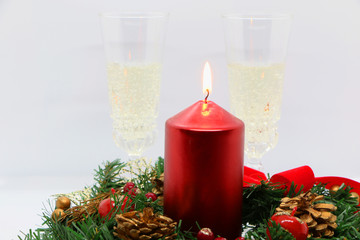 Two glasses of champagne, a red candle, a wreath on a white background.
