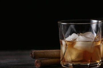 Glass of cold whiskey with cigars on wooden table against dark background