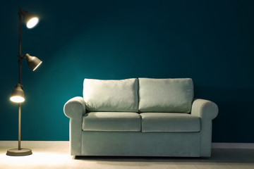 Comfortable sofa and lamp near color wall in room