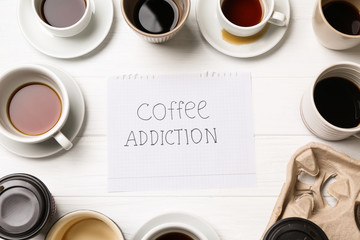 Almost empty cups of coffee and paper sheet with text COFFEE ADDICTION on table