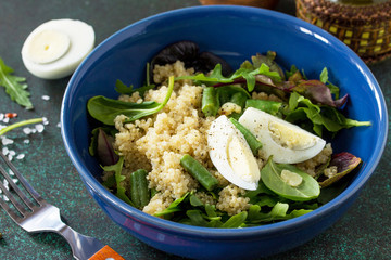 Diet menu close-up, Vegan food. Healthy salad with quinoa, green beans, eggs and salad dressing on a dark stone table.