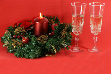 Two glasses of champagne, a red candle, a wreath on a red background.