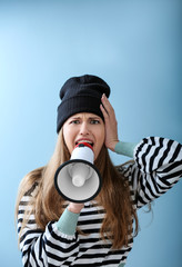 Shocked young woman with megaphone on color background