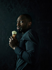 Portrait of sad afro american man holding ice cream over black studio background