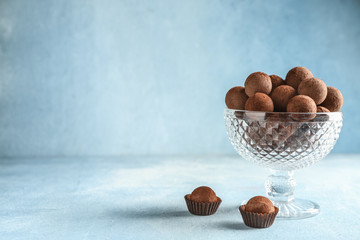 Glass bowl with sweet truffles on light background