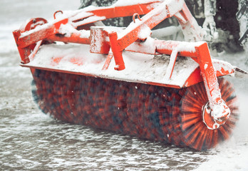 City service cleaning snow , a small tractor with a rotating brush clears a road in the city park...