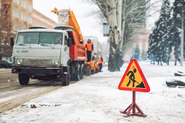 Snow-plow remove snow from the city street.Warning road sign.Winter service vehicle snow blower work.Cleaning snowy frozen roads.