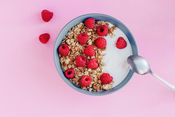 Healthy Breakfast yogurt with granola and raspberry on pink background top view copy space