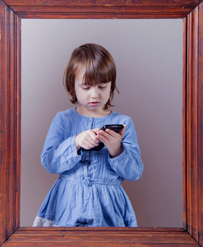 Using mobile phone as symbol of nothing seen, heard, said at the same time. Conceptual photo of little child girl with smart phone.