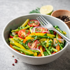 Salad with asparagus, bell pepper, cherry tomatoes, red onion and green peas in ceramic bowl on stone background. Top view. Copy space.