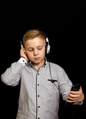 the boy listens to music with headphones and holding a mobile phone.