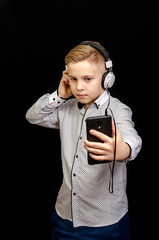 the boy listens to music with headphones and holding a mobile phone.