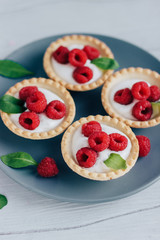 Tartlets with cream and raspberry on a grey plate