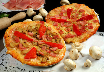 Imagen de dos pizzas con tomate, queso fundido, champiñones, jamón cocido y pimiento rojo.