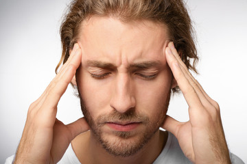 Young man suffering from headache on light background, closeup