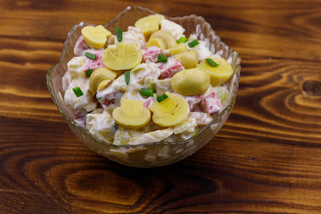 Potato salad with marinated mushrooms, sausage, onion and mayonnaise on wooden table