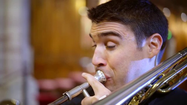 close-up shot of adult musician playing a song on a trombone in a catholic church.