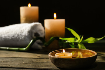 Bowl with water and burning candle on wooden table in spa salon