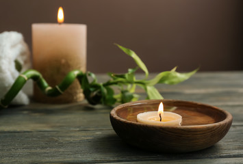 Fototapeta na wymiar Bowl with water and burning candle on wooden table in spa salon