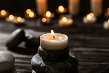 Spa stones and burning candle on wooden table
