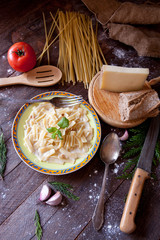 Carbonara noodles on a rustic table, kitchen cutlery, cheese, bread and tomato.