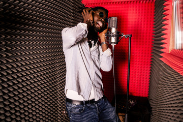 African man loudly singing a song in the recording Studio standing in front of the microphone....