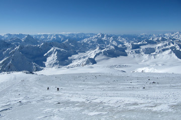Fototapeta na wymiar Beautiful views of the ridge and mountain peaks. Snowboarders go down the slope off the road.