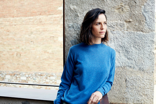 Junge Frau in blauem Pullover steht auf Balkon vor Steinwand