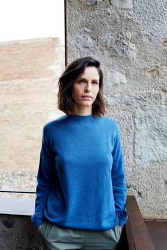 Junge Frau in blauem Pullover steht auf Balkon vor Steinwand