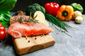 Raw salmon fillet and colorful vegetables on grey stone background.