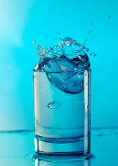 Pure drinking water with splashes in a round glass on a light green background