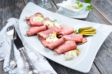 Traditional lunch meat with sliced cold cuts roast beef and remoulade as closeup on a white plate on a wooden table