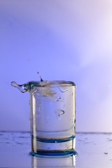 Pure drinking water with splashes in a round glass on a light Violet background