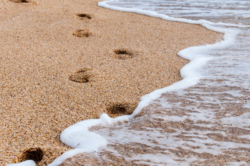 foam from the waves on the sea beach and footprints from the feet of a person
