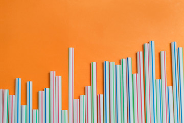 Striped drink straws of different colors in row isolated on orange background. Minimalism concept. Pop art style. Flat lay with straws used for drinking water or soft drinks. Copy