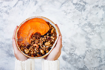Woman in woolen sweater holding bowl with cinnamon granola, coconut yogurt, chia seeds and pumpkin puree. Healthy vegan, vegetarian breakfast smoothie bowl