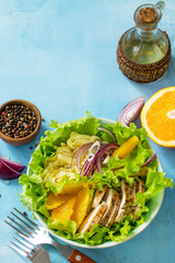 Diet menu. Healthy salad close-up, salad with chicken, egg pancakes, orange, green salad and dressing vinaigrette on a blue stone table. Copy space.