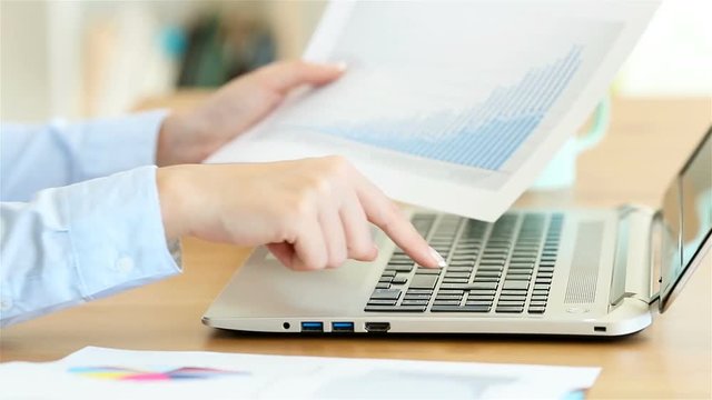 Close up of a office worker hands entering data in a laptop on a desktop