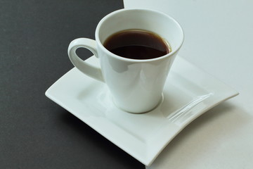 White and black. White porcelain cup with fragrant hot coffee on figured exclusive porcelain saucer. Contrast background.