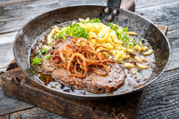 Traditional dry aged sliced roast beef with fried onion rings and Swabian spaetzle as closeup in a wrough-iron pan with brown sauce